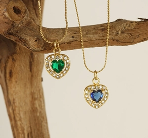 Detail of gold heart necklaces with green and blue crystals hanging on a branch