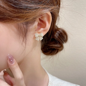 Elegant gold bow earrings featuring white pearls and crystals worn by a model