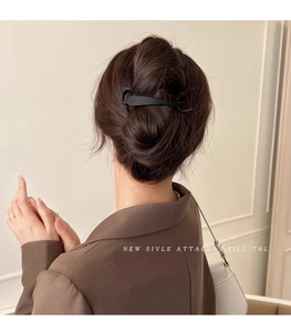 Close-up of a matte black large duckbill hair clip styling a low bun on a model