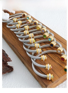 Macro detail of steel cable bangles featuring colorful inlaid stones on wooden display