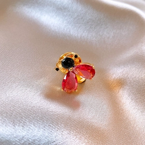 Detailed close-up of a 14k gold-plated bee brooch with red crystals on champagne silk