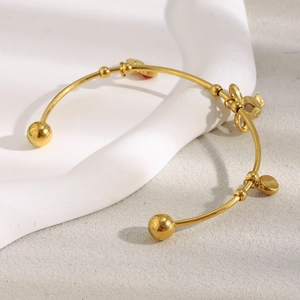 Détail du nœud doré 18K et du charm cœur rouge sur un jonc élégant en forme de C