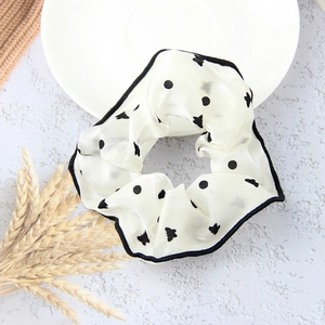 White chiffon scrunchie with black polka dots and butterfly patterns in a flat lay view