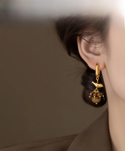 Detail of 18k gold bird earrings with tiger eye beads on female model
