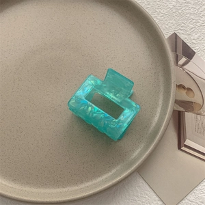 Dettaglio molletta per capelli quadrata con trama marmorizzata verde su piatto ceramico