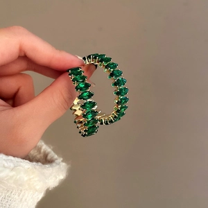 Detailed side view of large gold hoop earrings set with marquise-cut green emerald stones
