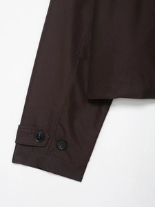 Detailaufnahme eines dunkelbraunen Trenchcoats mit Ärmelknöpfen und Köpergewebe-Textur