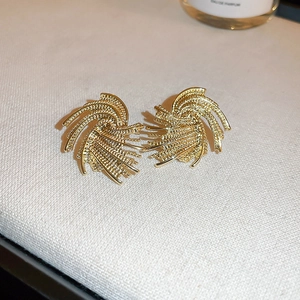 Close-up of vintage gold fan-shaped earrings with textured pearl details on beige fabric