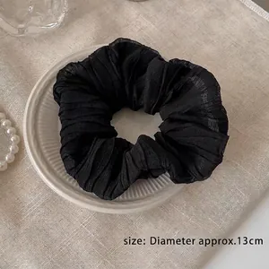 Detail of a large black pleated fabric hair scrunchie beside a white ceramic plate