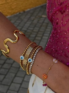 Close-up of stacked gold bracelets featuring evil eye, zircon tennis chain and bead charms