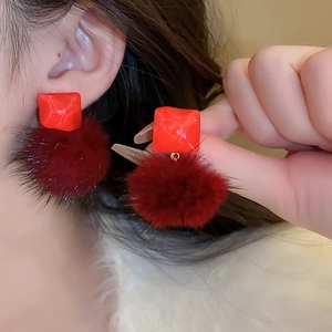 Close-up of red square resin and faux fur pompom earrings on a model for autumn