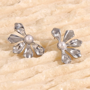 Macro shot of silver flower earrings with white pearl center on a textured stone surface