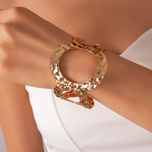 Detailansicht eines gehämmerten goldenen Armreifs mit geometrischem Hohldesign am Handgelenk