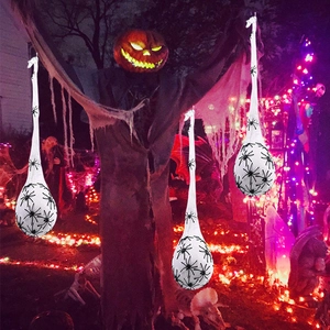 Luminous Halloween spider egg sacs hanging from a giant pumpkin prop in a night garden