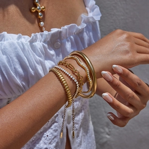 Gros plan de bracelets et chaînes empilables en acier inoxydable plaqué or 18 carats au poignet