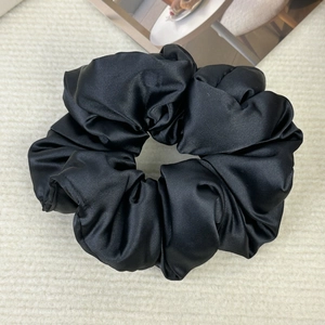 Detail of a large black satin scrunchie with soft pleated texture on a beige fabric background