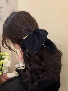 Detail of a large black jacquard bow hair tie with gold patterns on a half-up hairstyle