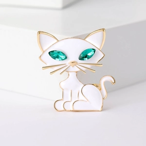 Detail of a white enamel cat brooch with emerald green gem eyes on golden finish