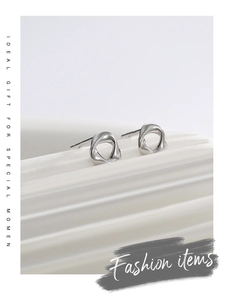Detailed macro view of minimalist twisted silver stud earrings on a wavy white base