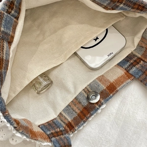 Detail view showing lace trim, magnetic clasp, and inner pocket of plaid tote bag