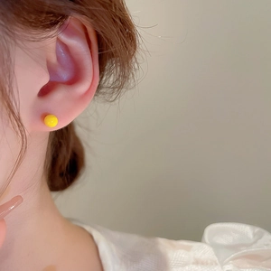 Close-up of a minimalist yellow round bead stud earring worn on a model's ear