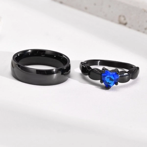 Detailed macro view of black stainless steel couple rings with a blue heart-shaped zircon