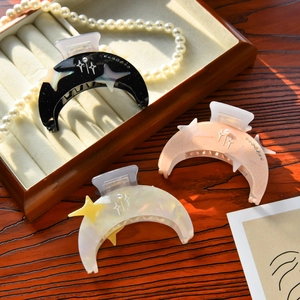 Detail of crescent moon hair claw clips with star patterns and pearl accents on a wooden desk