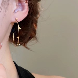 Close-up of gold irregular hoop earrings with triangular rivets worn by a model