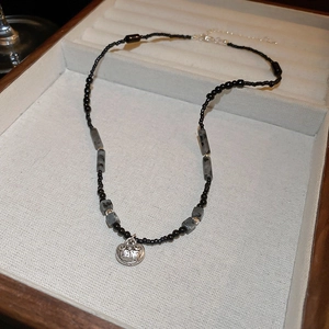 Close-up of black beaded necklace with a silver engraved circular pendant on a jewelry tray