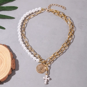 Close-up of double-layer necklace with gold chain, baroque pearl, coin and cross pendant