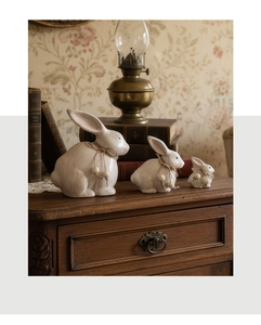 Dettaglio di tre statuine di conigli in legno vintage con fiocchi in lino su mobile