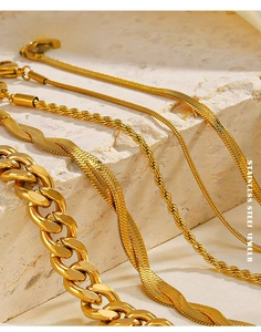 Close-up of gold stainless steel snake and cuban chains on minimalist stone props