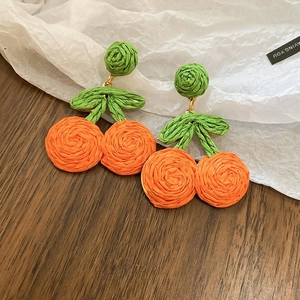 Detailed close-up of handmade woven orange fruit earrings with green leaves on gold hooks