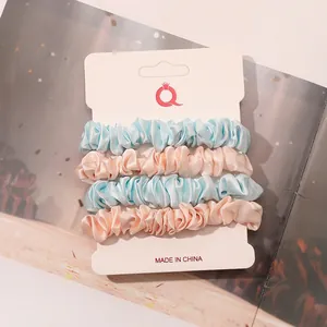 Detailed view of four satin silk scrunchies in blue and pink on display card