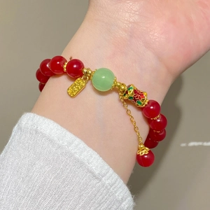 Détail d'un bracelet de perles rouges avec pierre verte et breloque dorée