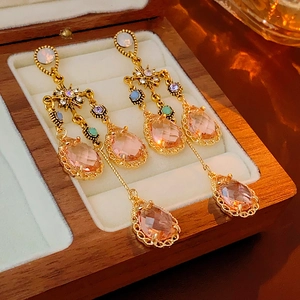 Close-up of vintage gold tassel earrings with pink teardrop gems in a wood jewelry box
