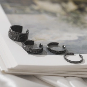 Detailed view of four black textured lava rings with matte finish on white book pages