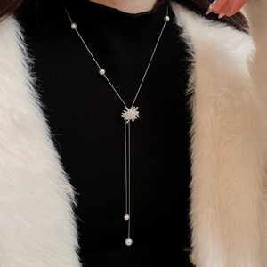 Collier pompon étoile et perle argentée sur un pull à col roulé noir et fausse fourrure