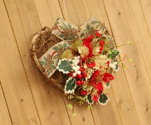 Close-up of heart-shaped Christmas wreath with red flowers and beige ribbon on wood