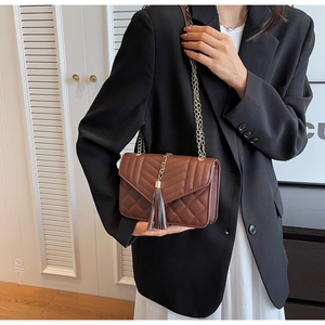 Detail of dark brown quilted crossbody bag featuring a golden chain strap and long tassel