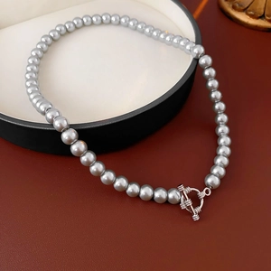 Detail of grey pearl necklace featuring a silver OT toggle clasp on a leather background
