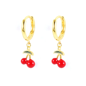 Macro detail of gold cherry hoop earrings with red fruit and green leaves on white background