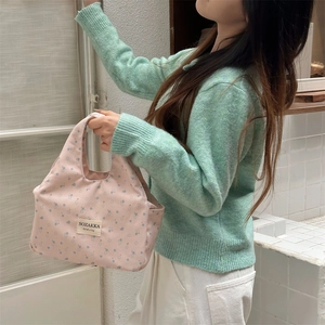 Detail view of a pink floral lunch bag with double handles and a stitched logo label