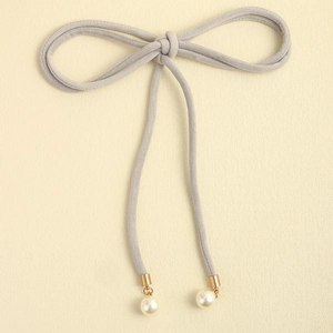 Detail of grey velvet bow belt featuring elegant white pearl pendants and golden metal caps