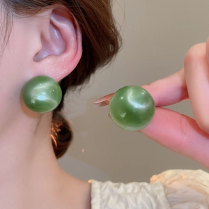 Detail of a large round green earring with a cat-eye stone texture on a female model