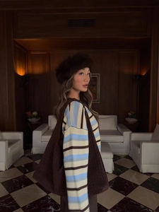 Detail of a blue and brown striped knit sweater styled with a woven bag and plush hat