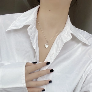 Close-up of heart-shaped silver pendant necklace worn on a model with white shirt