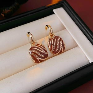Detail view of gold square zebra stripe enamel earrings with crystal inlay on white cushion