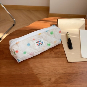 Detailed view of white quilted pencil case with colorful dots on a wooden table