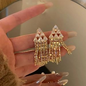 Macro shot of gold tassel earrings with triangular zircon studs and metal chain fringe